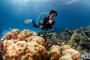 Asian male scuba diver swimming over tropical coral reef at Racha Island, a popular dive site near...