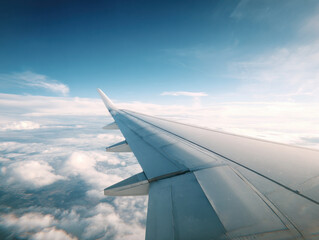 Fototapeta premium Aerial view of airplane wing above fluffy clouds and blue sky, evoking sense of freedom and adventure