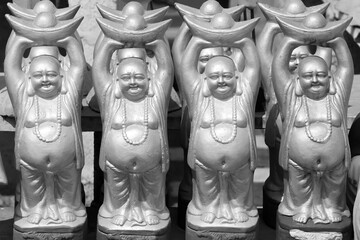 Many clay model laughing buddha statues up for sale in the market in rural India in monochrome.