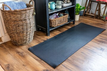 Black yoga mat on wood floor, beside wicker basket