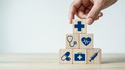 Hand stacking wooden blocks with medical symbols representing healthcare insurance and well being
