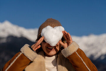 Snow Heart Woman Mountains: Winter fun, playful snow heart covering woman's eyes, joyful outdoor...