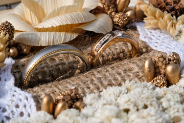 Close-up shot of a pair of gold wedding rings. Wedding ring or engagement ring in an aesthetic jewelry box containing dried decorative flowers, burlap and beads. Negative space