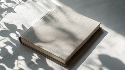 Soft shadows dance on a textured, closed book resting on a light surface in a serene setting