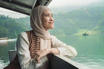 Asian muslim woman wearing hijab enjoys a serene moment on a boat, surrounded by lush greenery and...