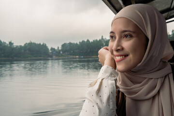Smiling Asian Woman in Hijab Relaxing by a Scenic Lakeside