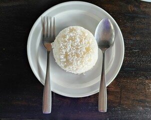 Rice in white plate with spoon and fork on black wooden table top view