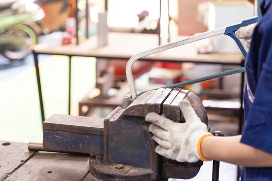 Closeup hand of industrial engineer use a handle saw to cut workpiece at industrial workshop.