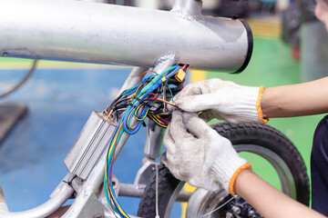 Closeup electrical engineer checks the wiring system to repair an electric bicycle in workshop.