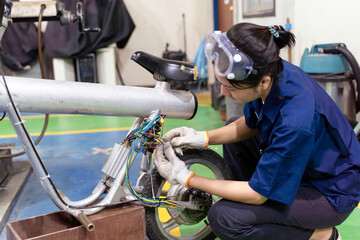 An Asian female electrical engineer checks the wiring system to repair an electric bicycle in workshop