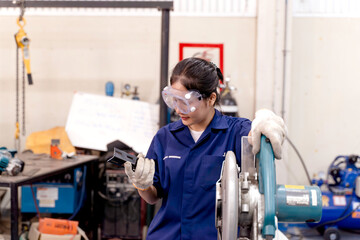Asian woman industrial engineer holds and inspects workpiece to check for neatness after using electric metal cutter to cut workpiece at industrial workshop.