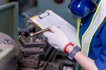 Closeup and clop hand of industrial engineer in uniform checking old model lathe and drilling machine and writing a maintenance playlist on clipboard at industrial workshop.