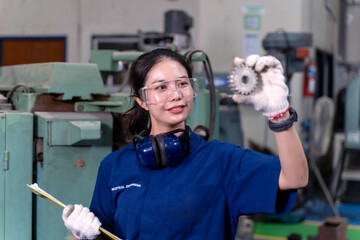 Closeup Asian woman technician engineer hold and looking check example small gear with clipboard at industrial workshop.