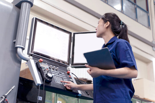 Asian woman industrial engineer in uniform look at screen display to check the system to activate automated cnc machinery in industrial workshop.