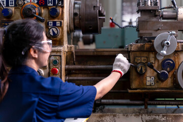 Closeup and back view of Asian woman industrial engineer in uniform working with old model lathe and drilling machine at industrial workshop.