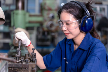 Closeup Asian woman industrial engineer in uniform working with old model lathe and drilling machine at industrial workshop.