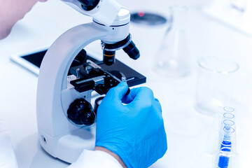 Closeup and crop hand of scientist adjust the tray level of microscope while working on medical research in science laboratory