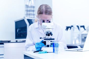 Woman scientist looking at science microscope medical test and research biology chemistry in the laboratory.