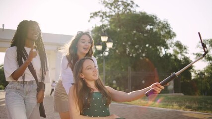 three multiracial female friends one disabled in a wheelchair enjoying a sunny day outdoors while capturing memories with a selfie stick in a park setting - Powered by Adobe