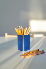 Yellow pencils in blue holder on white table with natural sunlight and shadows creating a peaceful workspace ambiance.