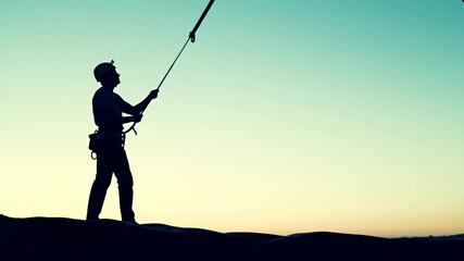 Climber silhouette pulls rope against a two-tone sky backdrop - Powered by Adobe