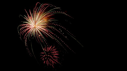 Fototapeta premium Two vibrant red, green and yellow fireworks bursting in a brilliant display against a black sky background with copy space.