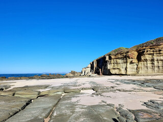 Eroded wave cut rock platform with exposed joint lines. Cliff in the background next to the ocean with a blue sky. Soldiers Point New South Wales Australia