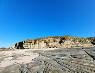 Eroded wave cut rock platform with exposed joint lines. Cliff in the background next to the ocean with a blue sky. Soldiers Point New South Wales Australia