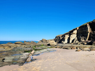 Eroded wave cut rock platform with exposed joint lines. Cliff in the background next to the ocean with a blue sky. Soldiers Point New South Wales Australia