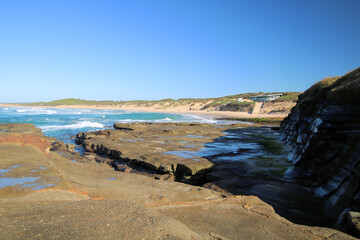 Eroded wave cut rock platform with exposed joint lines. Cliff in the background next to the ocean with a blue sky. Soldiers Point New South Wales Australia