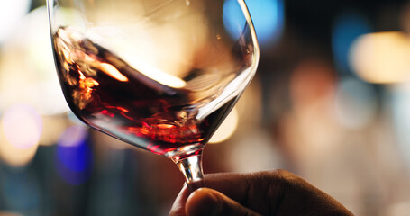Hand, person and swirl red wine in glass for taste testing, quality control and sensory ritual. Customer, inspection and alcohol for aroma, balance flavour and evaluation process and event with bokeh