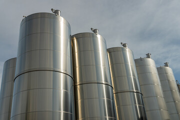 Gros plan de grandes cuves en inox photographiées en extérieur, illustrant leur surface métallique brillante et leur usage industriel.