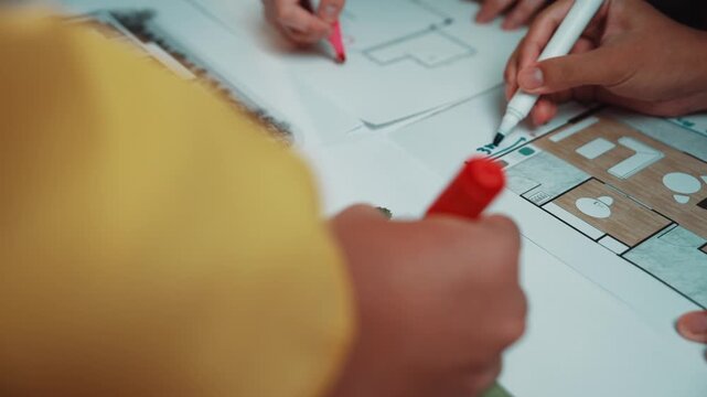 Two hands actively sketch on an architectural plan with colorful markers, representing a creative process in design and collaboration in a workspace. SACTR