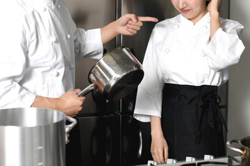 厨房で男性シェフから叱られる女性シェフ
