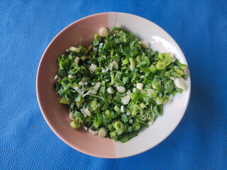 Chopped green onions in ceramic bowl isolated on blue background