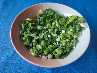 Chopped green onions in ceramic bowl isolated on blue background