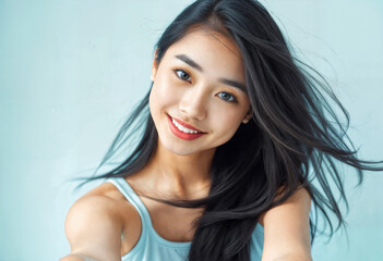 Smiling Asian Woman with Long Black Hair Against a Light Blue Background