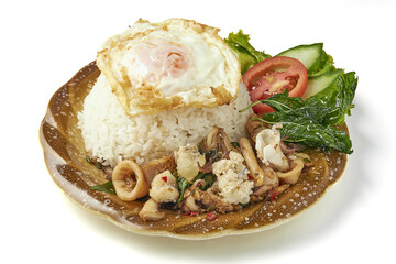 Stir fried squid with Thai holy basil served over steamed rice and topped with fried egg, garnished with fresh cucumber and tomato slices for flavorful and aromatic meal