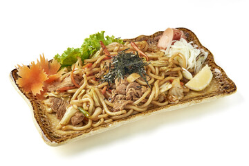 Stir fried yakisoba noodles with vegetables, beef, and garnishes served on ceramic plate, accompanied by pickled ginger, shredded radish, and lemon wedge for flavorful presentation
