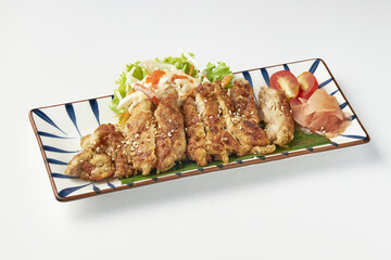 Crispy fried chicken served on rectangular plate with fresh salad, cherry tomatoes, pickled ginger,...