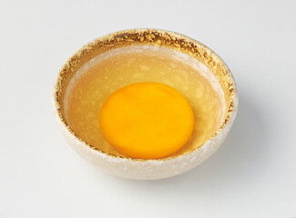 Single raw egg yolk in ceramic bowl with rustic design, placed on white background, showcasing its vibrant yellow color and smooth texture