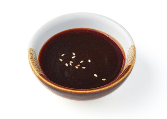 Small ceramic bowl filled with dark soy based dipping sauce, garnished with sesame seeds, isolated on white background. sauce appears rich and flavorful, perfect for enhancing dishes