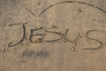 Jesus name written in the sand on a beach with a heart outline above
