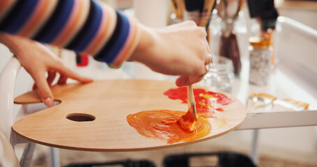Hands, paintbrush and palette with person in studio apartment for creative expression or...
