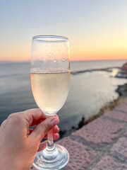 Hand Holds Sparkling wine or Champagne Glass at Sunset by Sea