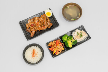 A savory beef rice bowl served as a set meal, featuring tender slices of beef simmered in soy-based sauce atop steamed white rice. The dish is accompanied by a variety of side vegetables and a light