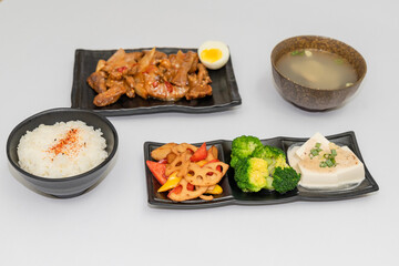 A savory beef rice bowl served as a set meal, featuring tender slices of beef simmered in soy-based sauce atop steamed white rice. The dish is accompanied by a variety of side vegetables and a light