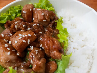 Chicken Teriyaki rice bowl with lettuce and sesame seeds above in wooden table background.
