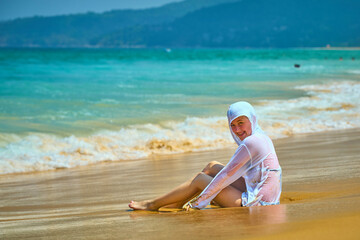a girl is sitting on a sandy beach, looking at the sea