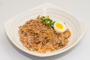 A savory beef rice bowl served as a set meal, featuring tender slices of beef simmered in soy-based sauce atop steamed white rice. The dish is accompanied by a variety of side vegetables and a light